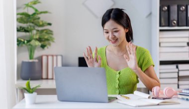 Modern bir iş kadını portresi, yeşil tişörtlü bir kadın ev ofisinde dizüstü bilgisayarla çalışıyor.