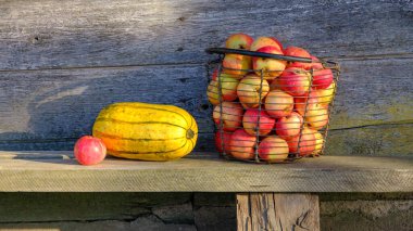 Eski ahşap bir evin arka planında kırmızı elma ve balkabağı dolu bir sepet..