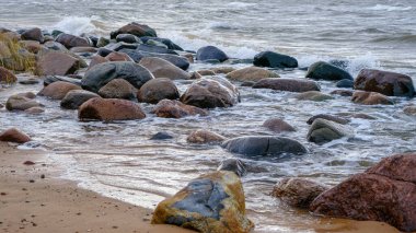 Baltık Denizi, gün batımında kayalar. Gece fırtınasından sonra küçük dalgalar.