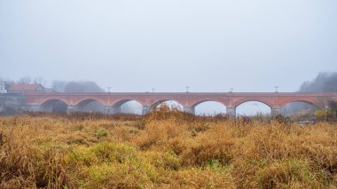 Sisli bir sonbahar gününde Letonya 'nın Kuldiga kentindeki Venta üzerinde kuldiga tuğla köprü. Doğa, eski kasaba mimarisi ve köprüsü olan güzel bir manzara..