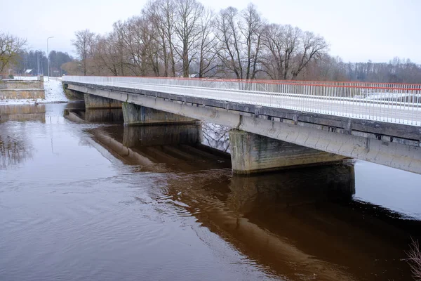 River Aiviekste in Vidzeme, Latvia in winter time. High water level in the river, dark January day. Bridge over the river.
