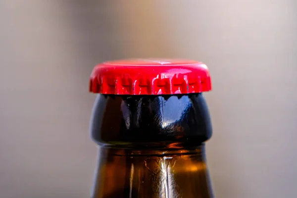 Brown glass beer bottle neck with red metal cap. close-up of unopened bottle.
