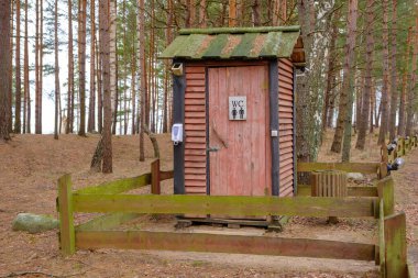 Professionally, qualitatively built wooden toilet in nature. Communal building for tourists in the forest. A fence of wooden planks surrounds the building.
