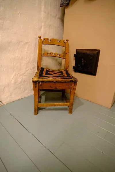 古い木製の椅子 ストーブのそばに木製の椅子が置かれている 椅子の上にニット生地が置かれています — ストック写真