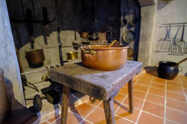 Eski pirinç kaplar. Ortaçağ metal yemek pişirme aletleri. Eski bir şatonun mutfağının içi. Bir tencere ahşap bir tabureye konur. Letonya Bauska Kalesi.