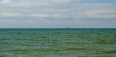 Ufuk çizgisine çok yakın beyaz bir yat mavi denizde tek başına yol alıyor. ve güzel mavi gökyüzü arka plan olarak kullanılacak. Baltık Denizi Letonya.