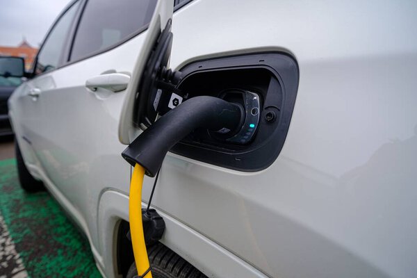 Съемка белого автомобиля, заправляющего бензин форсункой автомата на заправке.