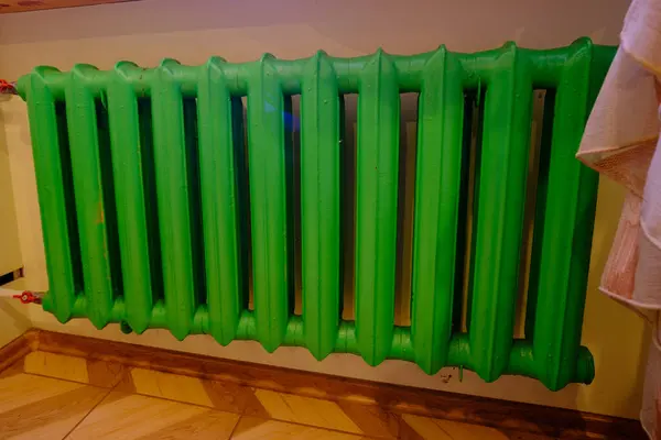 Old green color cast iron radiator heating on a background of an orange wall