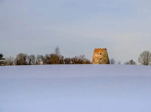 An old stone mill in a snow-covered field