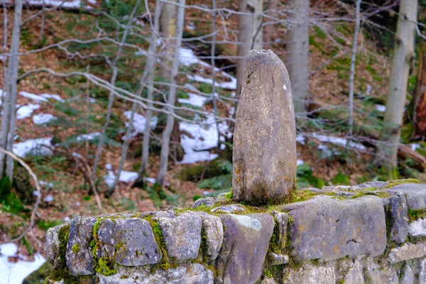 Old stone fence in the forest. One stone is placed vertically on the fence.