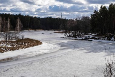 Yoğun bir ormanla çevrili donmuş bir nehirle sakin bir kış manzarası.