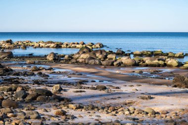 Berrak mavi gökyüzünün altında sakin suları olan sakin kayalık bir sahil..
