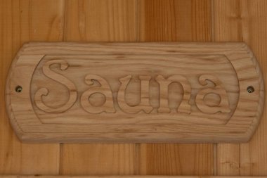 A wooden sign with the word Sauna carved into it, mounted on a wooden wall, indicating a sauna room.