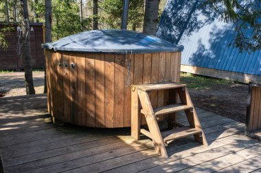 Ormanlık alandaki ahşap bir güvertede basamakları olan, rahatlamak ve doğaya dalmak için ideal, ahşap bir jakuzi..