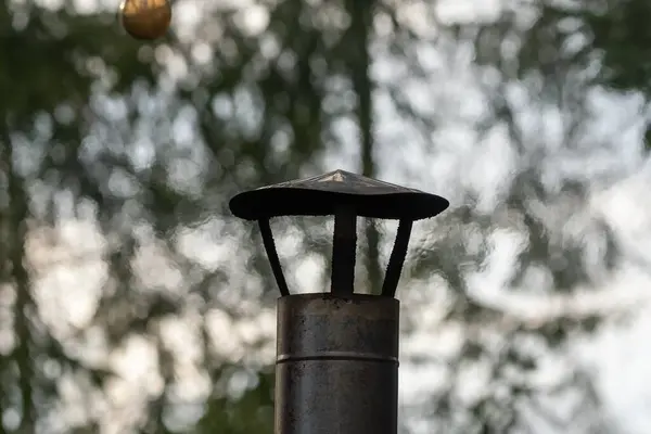 stock image A close-up view of a rustic metal chimney cap against a blurred background of trees, highlighting an outdoor forest setting and old craftsmanship.