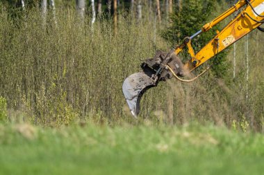 Close-up of an excavator arm and bucket actively digging in a forested area, highlighting construction and land development.