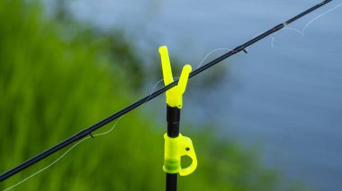 Neon sarısı bir tutucu tarafından korunan bir oltaya yakın plan su ve yeşil bitki örtüsüne karşı kurulmuş..