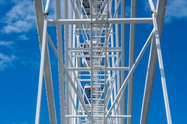 Dönme dolabın detaylı görüntüsü beyaz metal iskelet, açık mavi gökyüzüne karşı dağınık bulutlar.