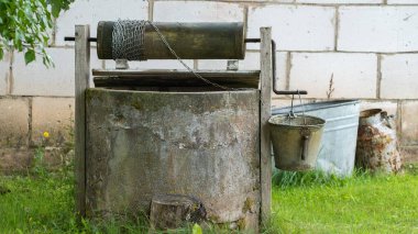 Zincirinde metal bir kova olan taşralı bir kuyu. Etrafı yeşillikle çevrili tuğla bir duvara dayanıyor..