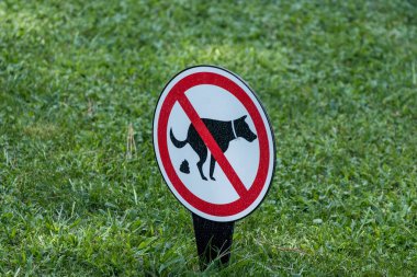 Çimenli bir çimenlikte köpek leşi bulunmayan bir tabelanın yakın plan çekimi. Evcil hayvan sahiplerinin köpeklerinin bölgeye pislemesini yasaklıyor..