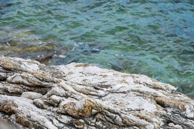 Engebeli kayalık kıyı şeridi kristal berrak turkuaz suyla buluşur, kıyı dokularının ve sakin denizin doğal güzelliğini gözler önüne serer..