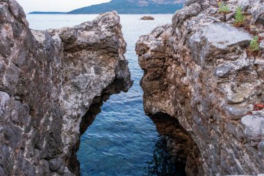 Doğal bir kaya yarığı sakin mavi sulara açılır ve engebeli kayalar ile dingin deniz arasında çarpıcı bir kontrastlık yaratır..