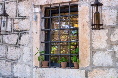 A rustic stone wall featuring a window with metal bars, decorated with small potted plants on the windowsill and lanterns hanging nearby. clipart