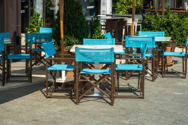 A vibrant outdoor cafe setup featuring bright blue chairs and tables, surrounded by greenery, creating a modern and inviting atmosphere. clipart