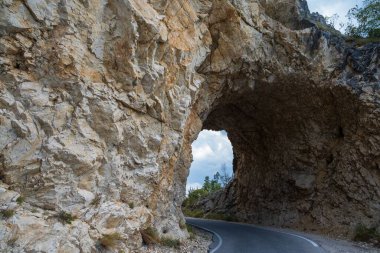 Dar, dolambaçlı bir yol kayalık bir dağa oyulmuş doğal bir tünelden geçer, engebeli araziler ve maceralar sergiler..