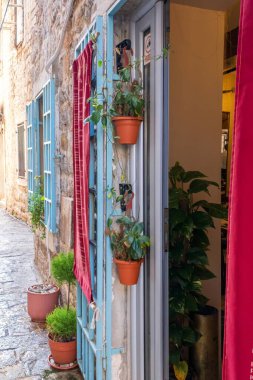 A cozy alleyway featuring blue shutters, potted plants, and red curtains, creating a welcoming atmosphere in an old town. clipart