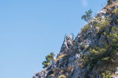 Engebeli kayalık bir uçurum, seyrek bitki örtüsüyle, parlak mavi gökyüzüne tutulmuş, saf güzellikleri ve araziyi gözler önüne seriyor..