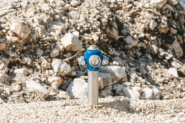 stock image A blue fire hydrant stands in front of a rugged, rocky backdrop, highlighting its industrial presence in nature.