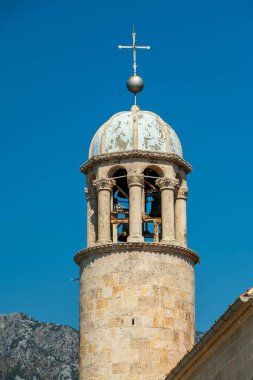 Kotor Körfezi, Karadağ - 22 Ağustos 2024: Açık mavi gökyüzüne karşı uzanan yıpranmış kubbesi ve haçı olan tarihi bir taş kilise çan kulesinin ayrıntılı bir görüntüsü.