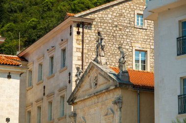 Kotor Körfezi, Karadağ - 22 Ağustos 2024: Taş heykeller, modern ve geleneksel yapılara karşı inşa edilmiş, kırmızı kiremitli ve klasik mimarisi olan tarihi bir taş binanın çatısını süslüyor.