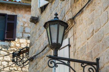 Kotor Körfezi, Karadağ - 22 Ağustos 2024: Taştan bir duvara monte edilmiş, kırsal pencere ve kablolarla çevrili, tarihi bir sokak dekorunun cazibesini yakalayan siyah bir eski fener.