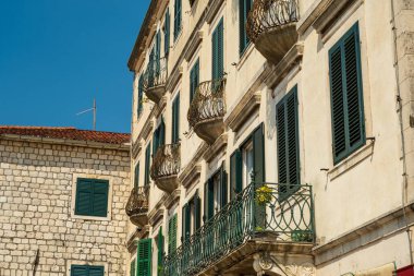 Kotor Körfezi, Karadağ - 22 Ağustos 2024: Açık mavi gökyüzünün altında yeşil pencereleri, süslü balkonları ve taş duvarları olan büyüleyici bir Akdeniz binası.