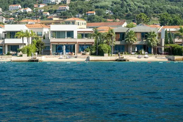 Kotor Körfezi, Karadağ - 22 Ağustos 2024: Sahil kenarındaki modern villalar, sakin bir sahil ortamında kurulmuş lüks konforlar ve çarpıcı deniz manzaraları sunuyor.