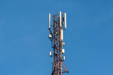 Telekomünikasyon baz istasyonu, anten ve ekipmanla, açık mavi gökyüzüne karşı kurulmuş, modern iletişim teknolojisini temsil ediyor..