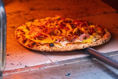 Close-up of a freshly baked pizza with toppings, cooking in a traditional wood-fired oven, showcasing golden crust and vibrant ingredients. clipart