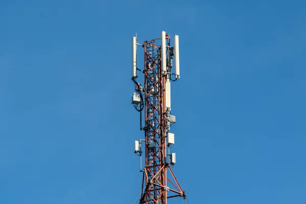 Telekomünikasyon baz istasyonu, anten ve ekipmanla, açık mavi gökyüzüne karşı kurulmuş, modern iletişim teknolojisini temsil ediyor..