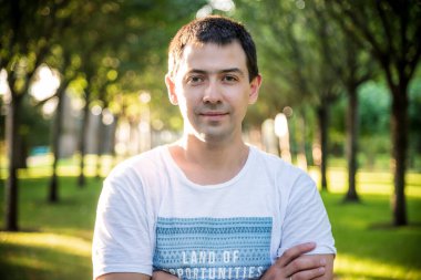 Açık havada beyaz gömlekli, doğa parkında gülümseyen güzel bir adamın portresini kapat. Moda modeli.