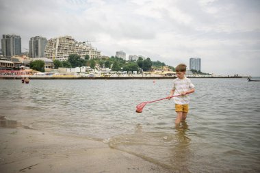 Küçük bir çocuk tek başına deniz kıyısına doğru yürüyen dalgalarla kumsalı keşfediyor. Mutlu çocukluk kavramı.