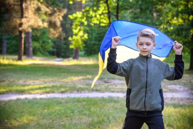 Ukrayna için dua et. Yaz parkını yöneten Ukrayna bayrağı taşıyan bir çocuk. Ulusal bayrak sallayan küçük çocuk barış için dua ediyor. Bağımsızlık Günü 'nü kutlayan mutlu çocuk.