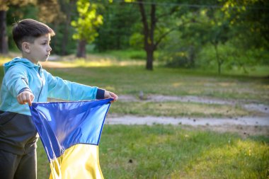 Ukrayna için dua et. Yaz parkını yöneten Ukrayna bayrağı taşıyan bir çocuk. Ulusal bayrak sallayan küçük çocuk barış için dua ediyor. Bağımsızlık Günü 'nü kutlayan mutlu çocuk.