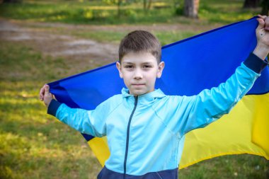 Ukrayna için dua et. Yaz parkını yöneten Ukrayna bayrağı taşıyan bir çocuk. Ulusal bayrak sallayan küçük çocuk barış için dua ediyor. Bağımsızlık Günü 'nü kutlayan mutlu çocuk.