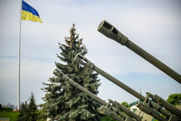 stock image Groups of ancient military guns against the background of the State Flag of Ukraine. Muzzle brake of an artillery gun. Sunny morning sky. Call to stop violence concept. Ukrainian flag.