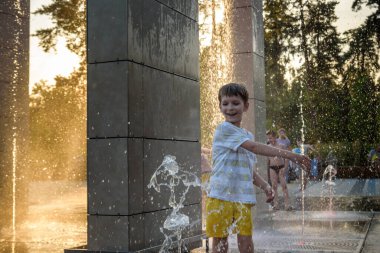 Çocuk çeşmelerde eğleniyor. Sıcak bir yaz gününde şehir çeşmesiyle oynayan bir çocuk. Fıskiyede eğlenen mutlu çocuklar. Yaz havası. Aktif eğlence, yaşam tarzı ve tatil.