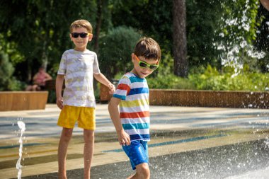 Çocuk çeşmelerde eğleniyor. Sıcak bir yaz gününde şehir çeşmesiyle oynayan bir çocuk. Fıskiyede eğlenen mutlu çocuklar. Yaz havası. Aktif eğlence, yaşam tarzı ve tatil.