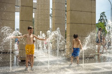 Boy having fun in water fountains. Child playing with a city fountain on hot summer day. Happy kids having fun in fountain. Summer weather. Active leisure, lifestyle and vacation.