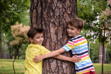 İki küçük çocuk bir ağaç gövdesine sarılıyor - çocuklar doğayı seviyor, sürdürülebilirlik kavramını. Doğayı kurtar..